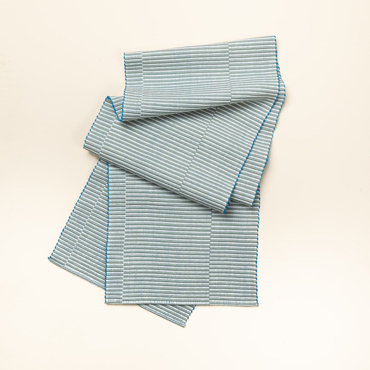 A table runner with offset stripe design that is hand woven in sage and blue colors. 