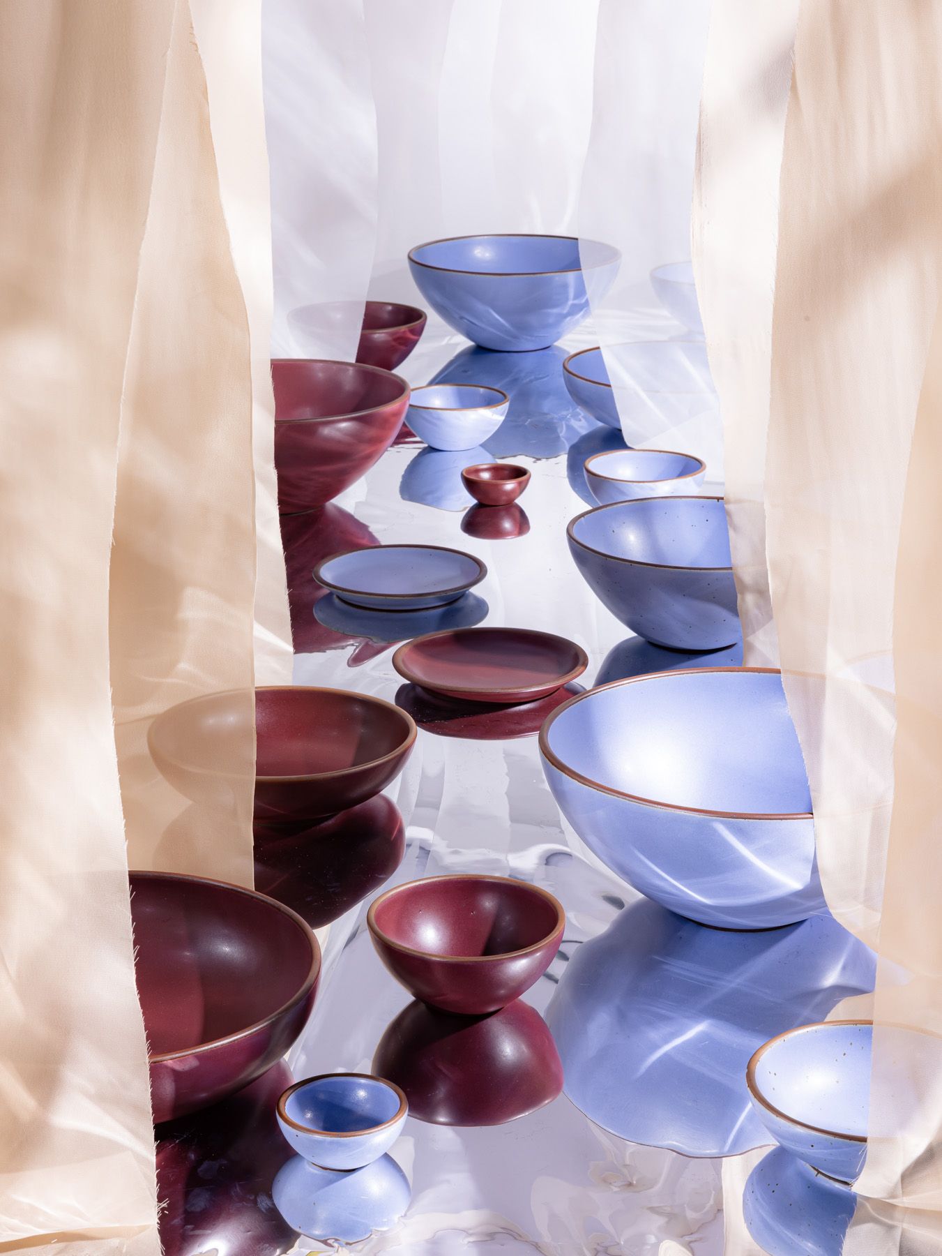 Ceramic plates and bowls in periwinkle and plum colors are artfully arranged against fabric and a reflective material