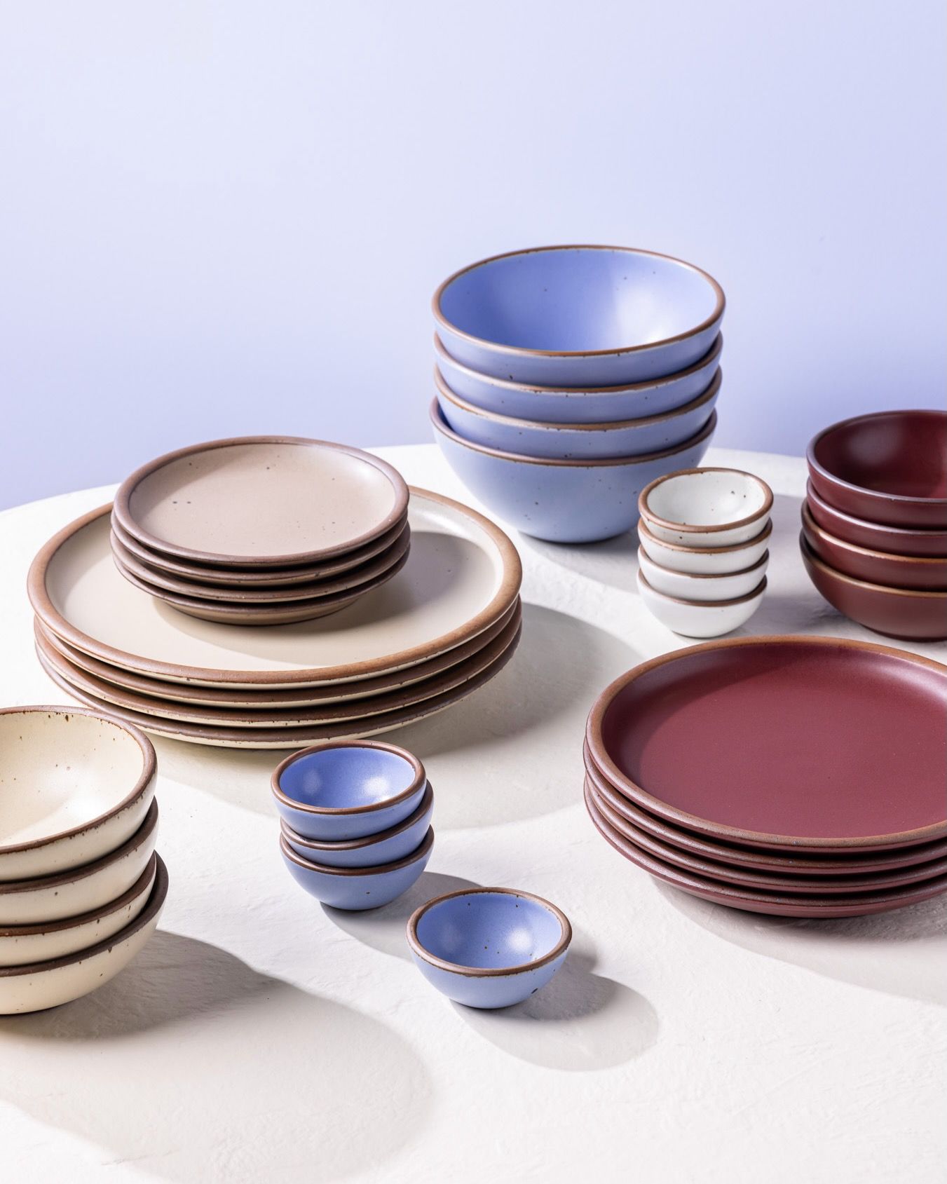 Stacks of ceramic plates and bowls in periwinkle, plum, white, and a light tan color
