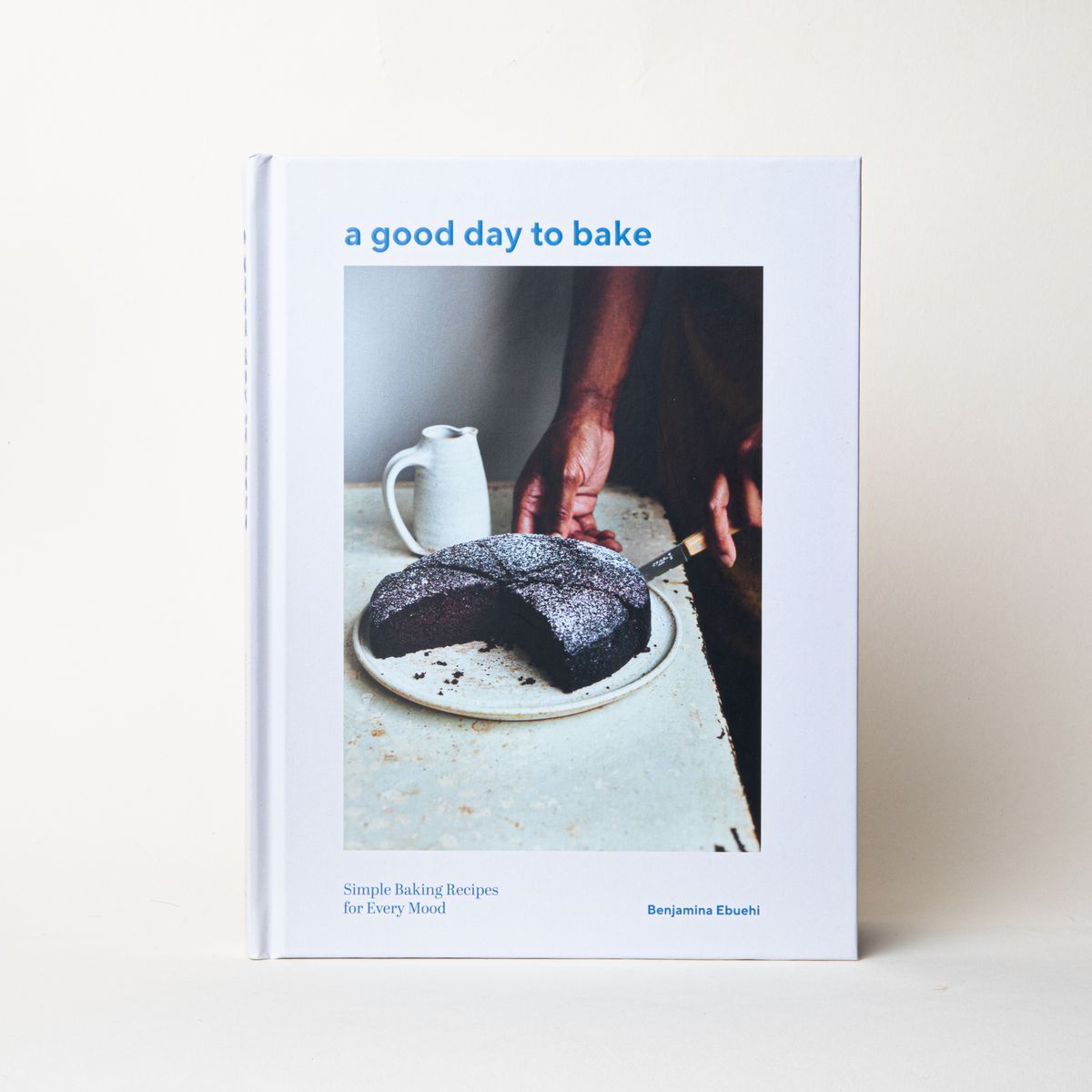 A book with a white cover and a large photo of a person cutting a cake with a title that reads "a good day to bake"