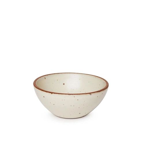 A medium rounded ceramic bowl in a warm, tan-toned, off-white color featuring iron speckles and an unglazed rim