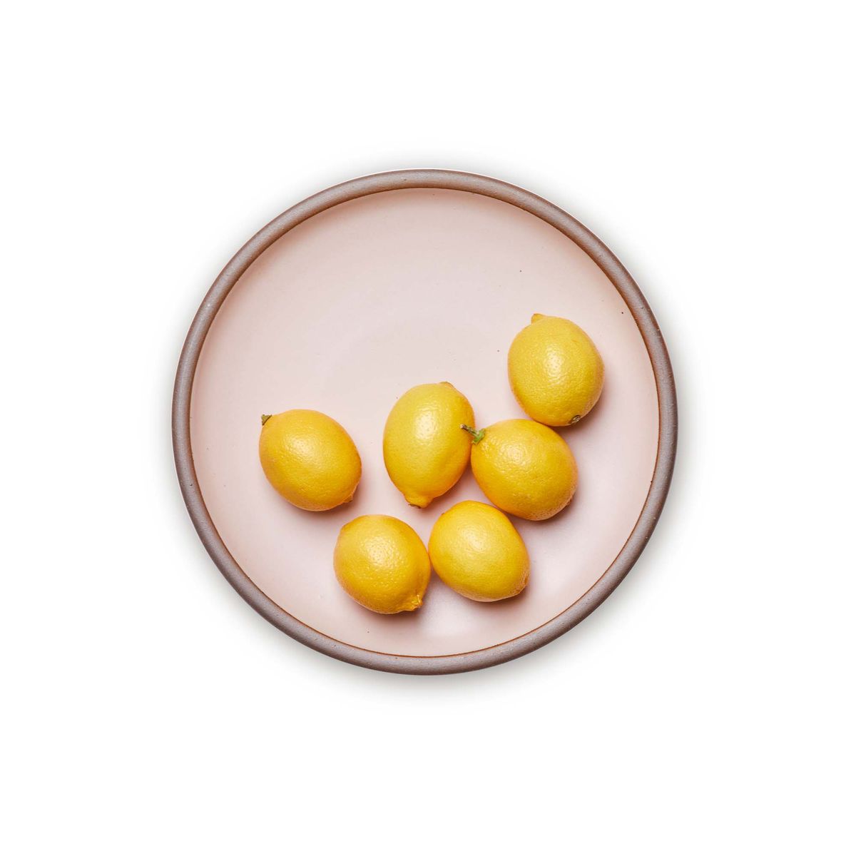 Lemons on a dinner sized ceramic plate in a soft light pink color featuring iron speckles and an unglazed rim