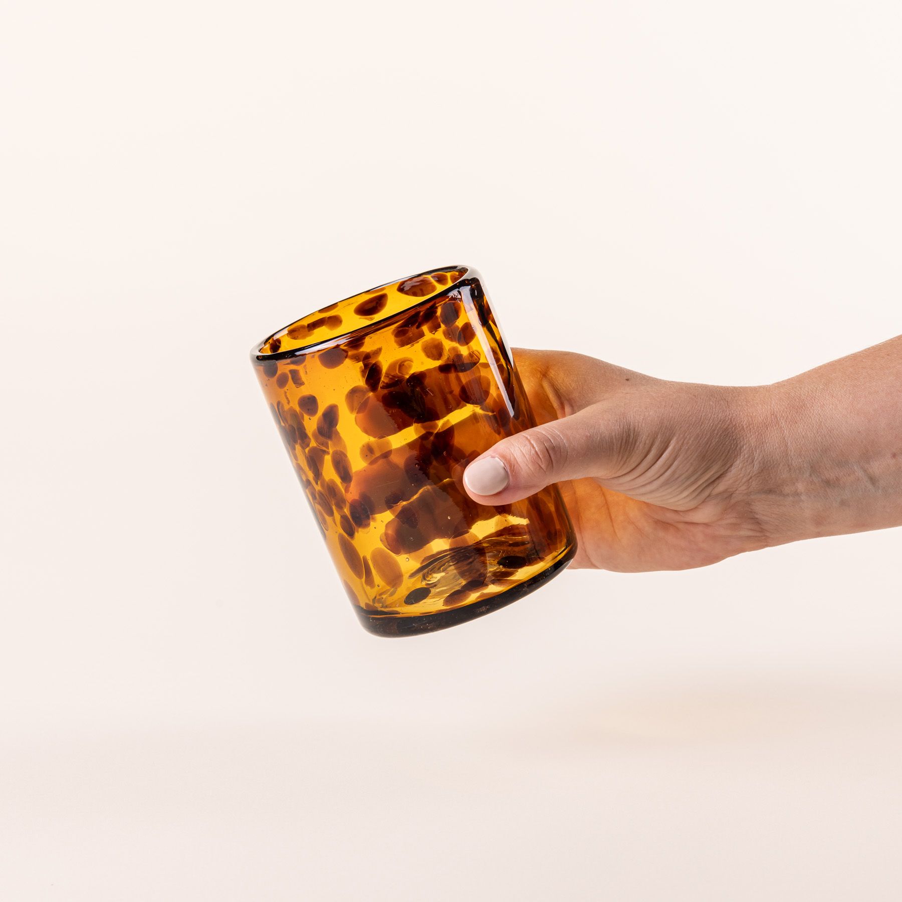 A hand holding a short tortoiseshell drinking glass