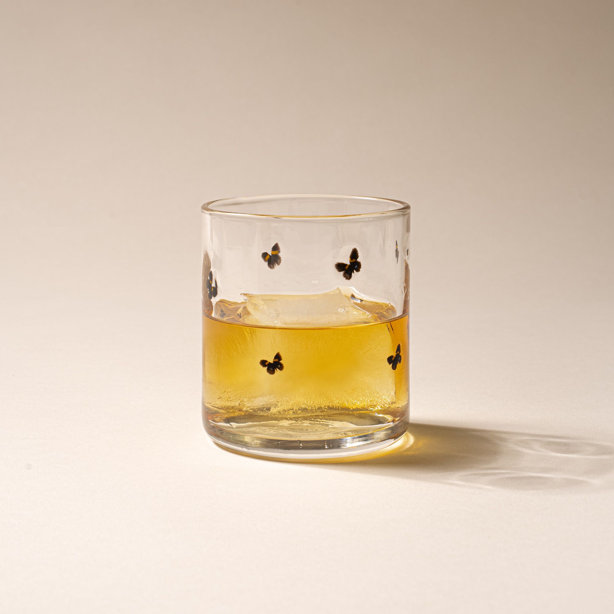 Clear glass with a ring of butterflies on a cream background, with a drink inside.