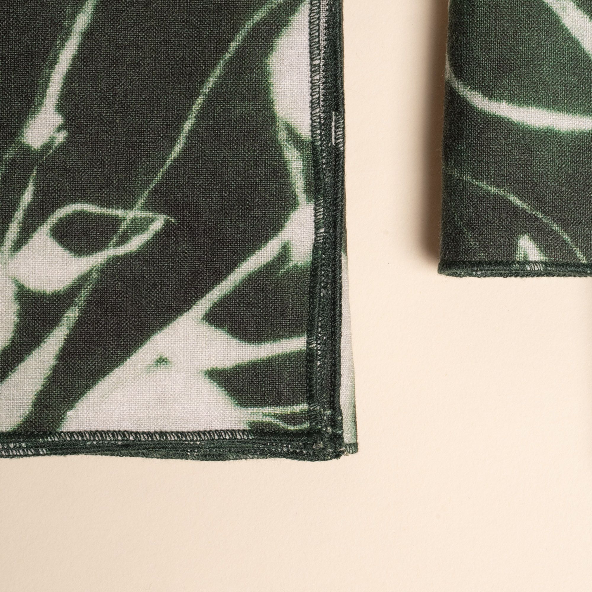 A close up of the corner of a dark green napkins with white botanical print, neatly folded on a neutral background.