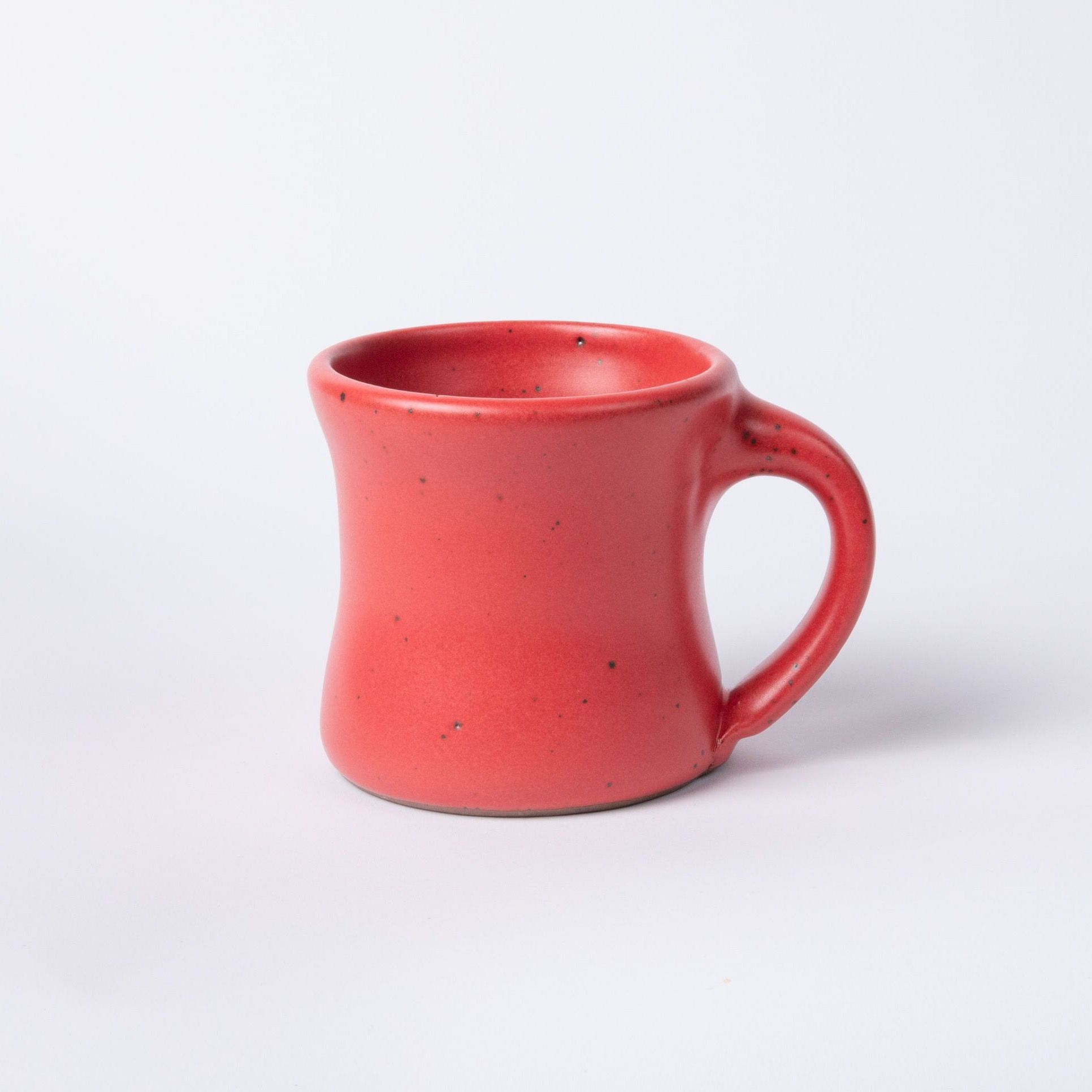 A classic diner mug that tapers out on the top and bottom in a bold red color featuring iron speckles and a handle.