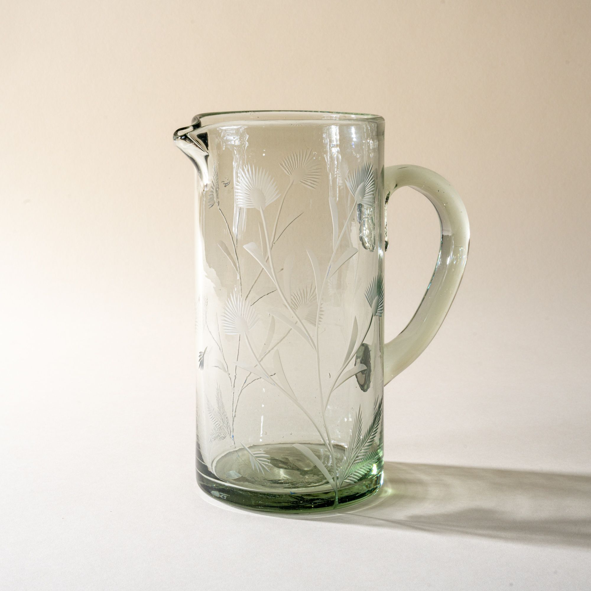 A large glass pitcher with handle made of recycled glass with etched thistle designs on it