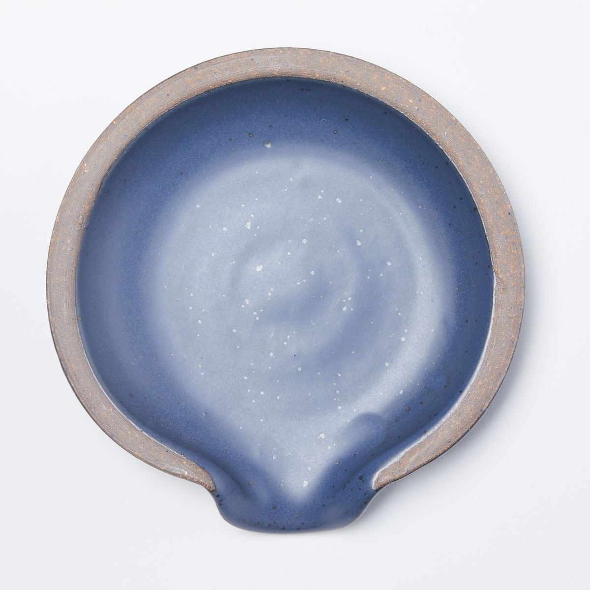 A circular ceramic spoon rest in a muted navy color featuring iron speckles and unglazed ridge rim