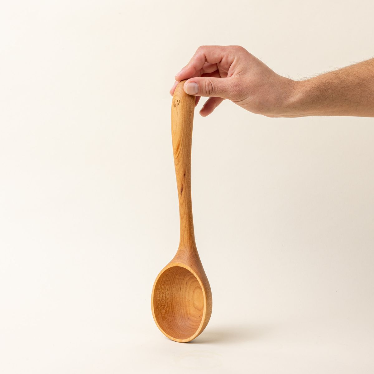 A hand holds a wooden ladle with a large scoop