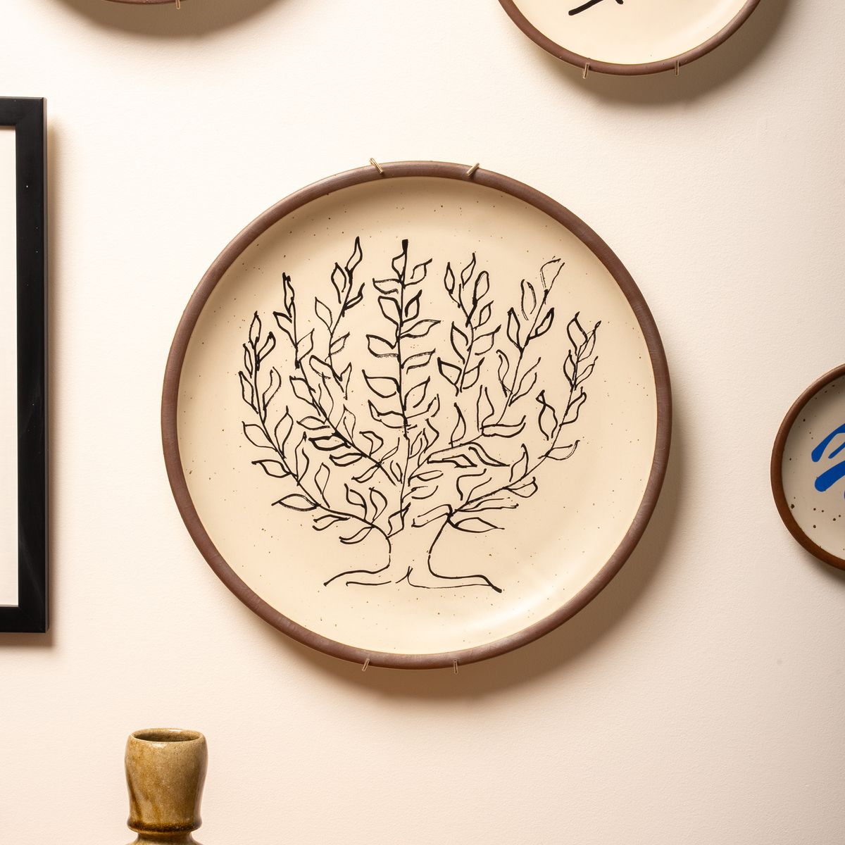 A large serving platter hangs on the wall in a brass plate hanger. The plate has a decal of the artwork, Le Platane by Henri Matisse.