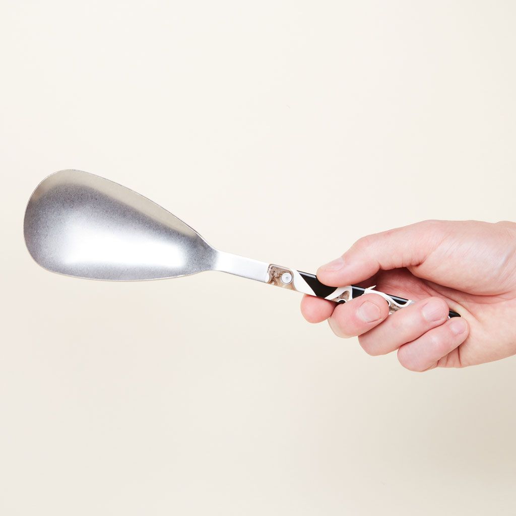 A hand holds a serving spoon with an elongated silver-colored bowl with a brown and white 