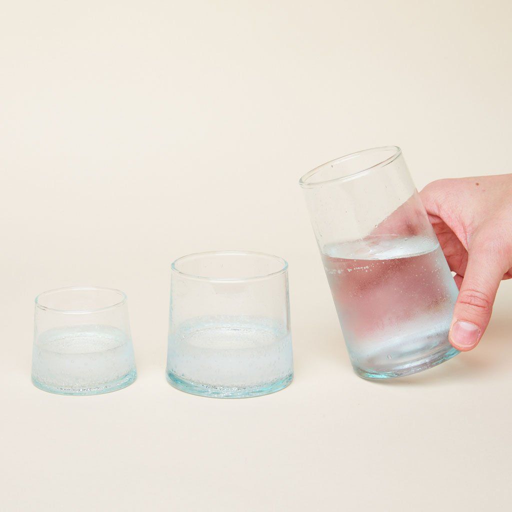 Recycled Moroccan glassware in short, medium, half-filled with clear bubbly liquid