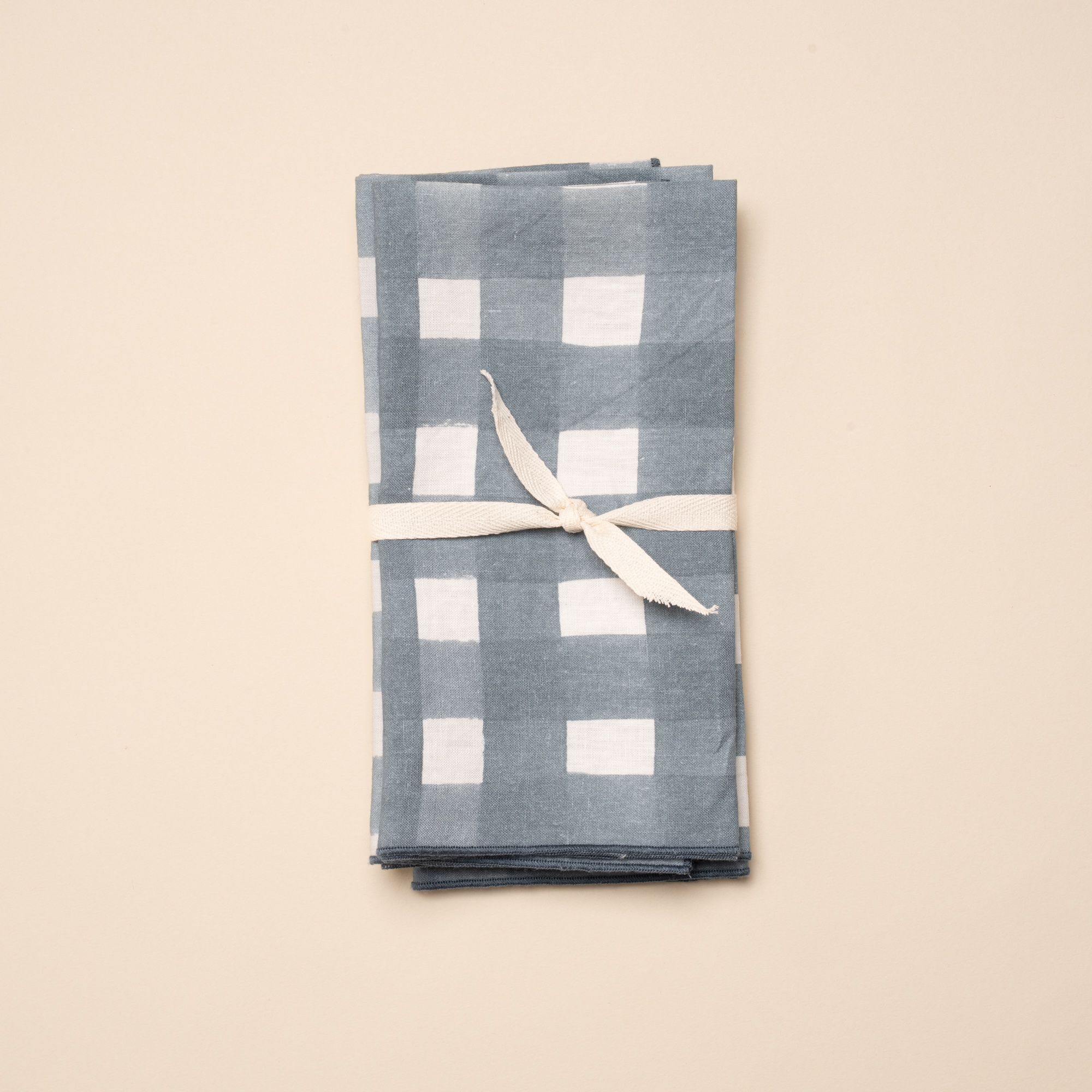 A stack of folded napkins with a blue-grey crosshatch pattern and an ivory ribbon wrapped around.