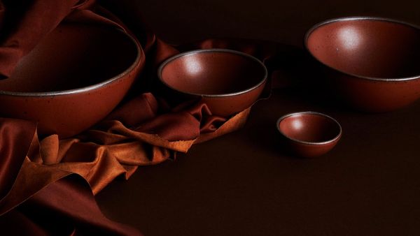 A moody photo of various ceramic bowls in a burnt terracotta color with fabric to match