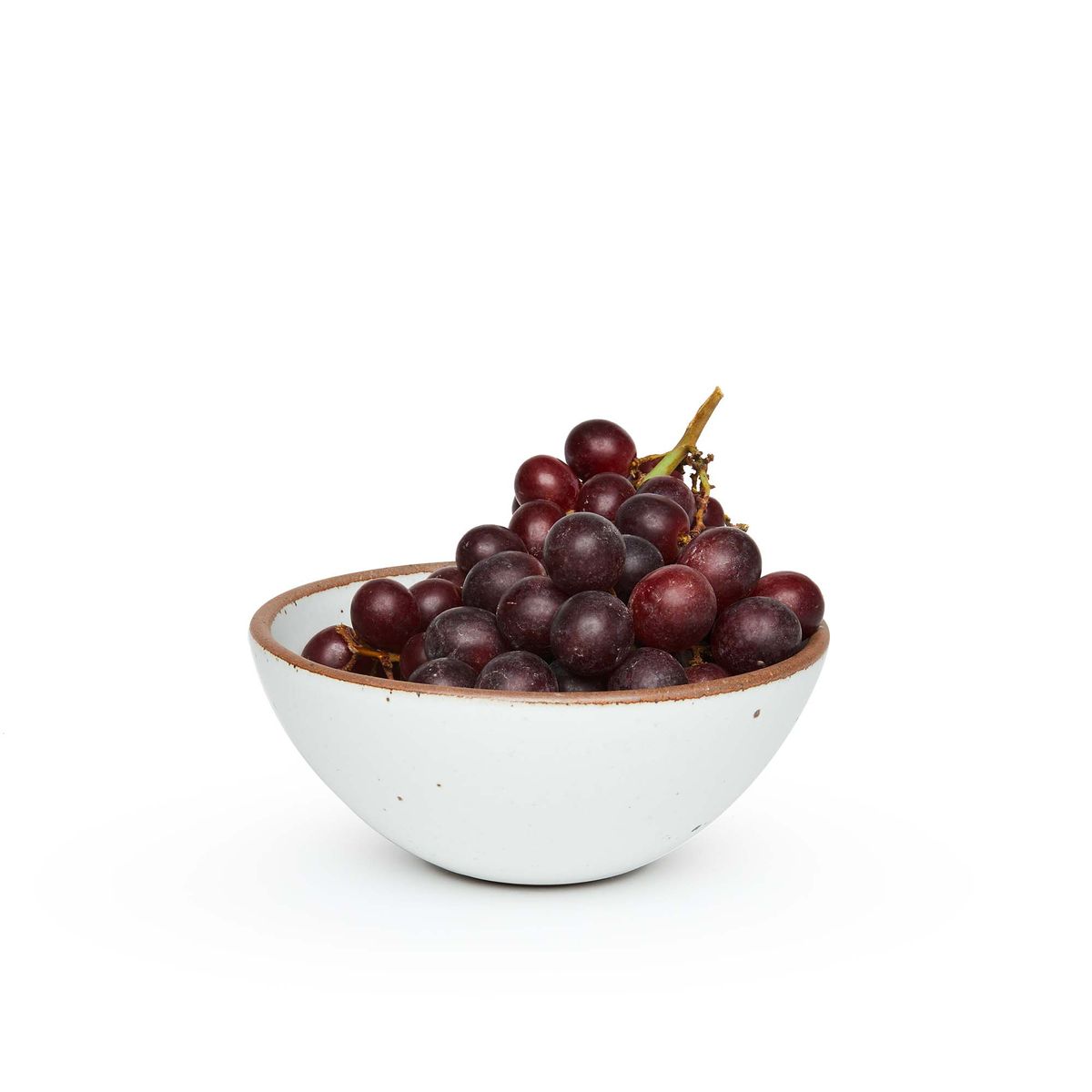 A medium rounded ceramic bowl in a cool white color featuring iron speckles and an unglazed rim, filled with grapes