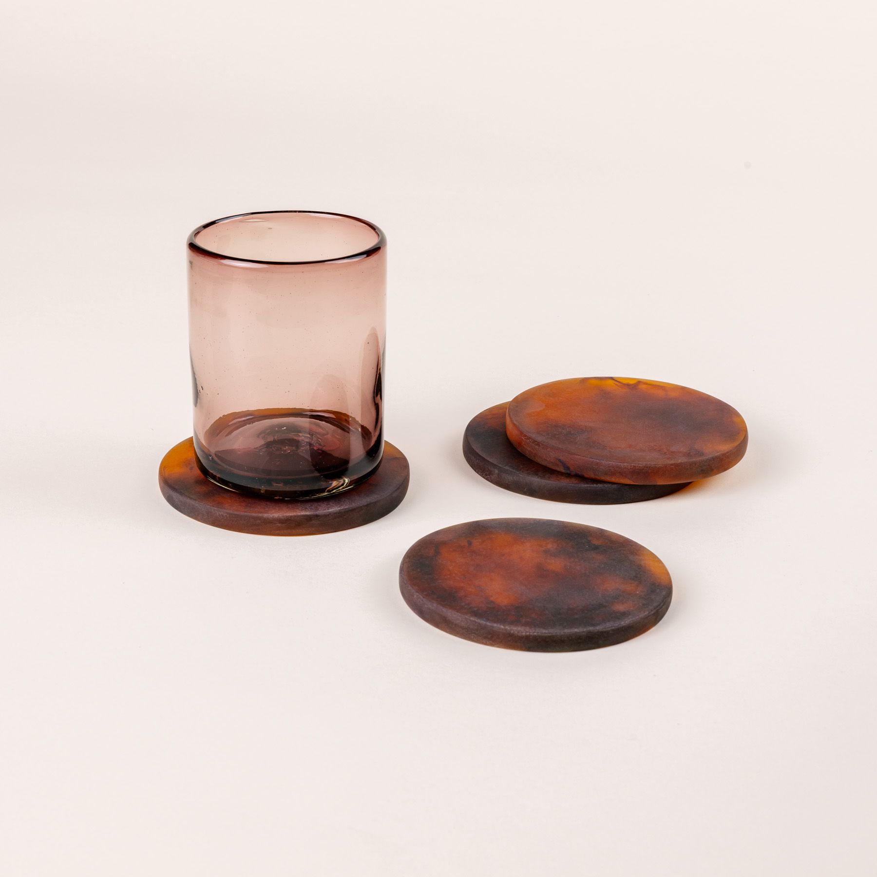 4 circular tortoiseshell coasters with 1 light pink tumbler glass sitting on one.