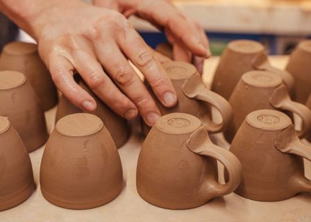 John placing a thrown espresso cup on a piece of wood to dry with rows of other espresso cups