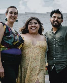 Outside, three people are standing close together smiling at the camera