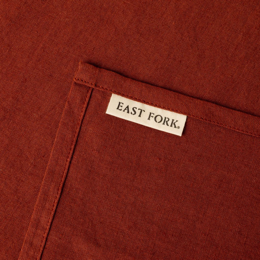 A terracotta linen napkin close up of texture and sewn-in corner tag that reads "East Fork"