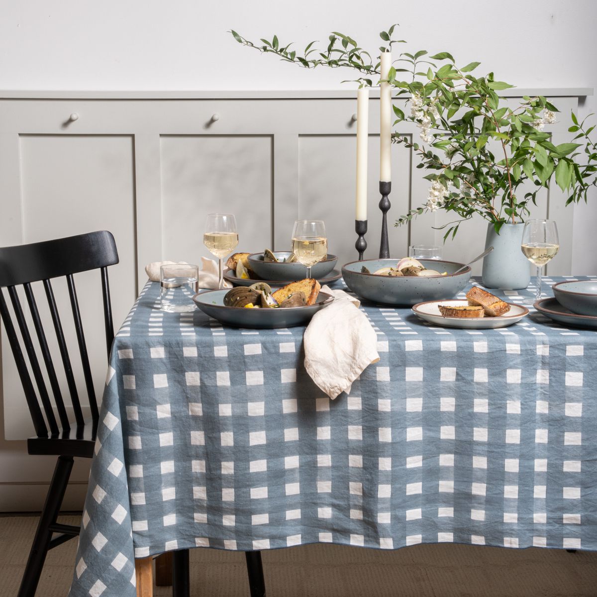 A table featuring a blue-grey crosshatch pattern, blue-grey ceramic dinnerware, wine glasses, iron candlesticks and more.