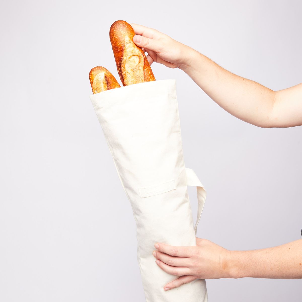 Hand pulling a baguette out of a cotton bread bag