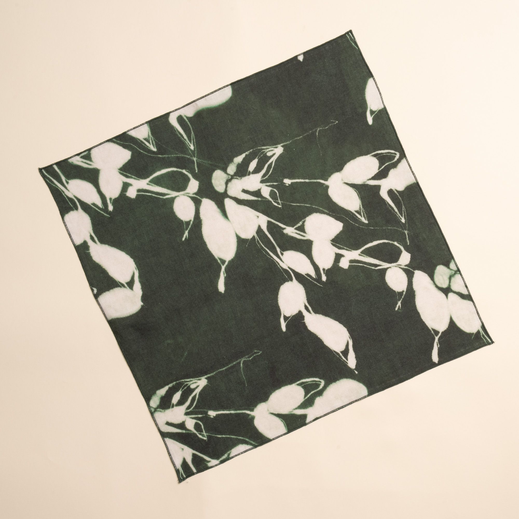 A square dark green napkin with white botanical print on a neutral background.