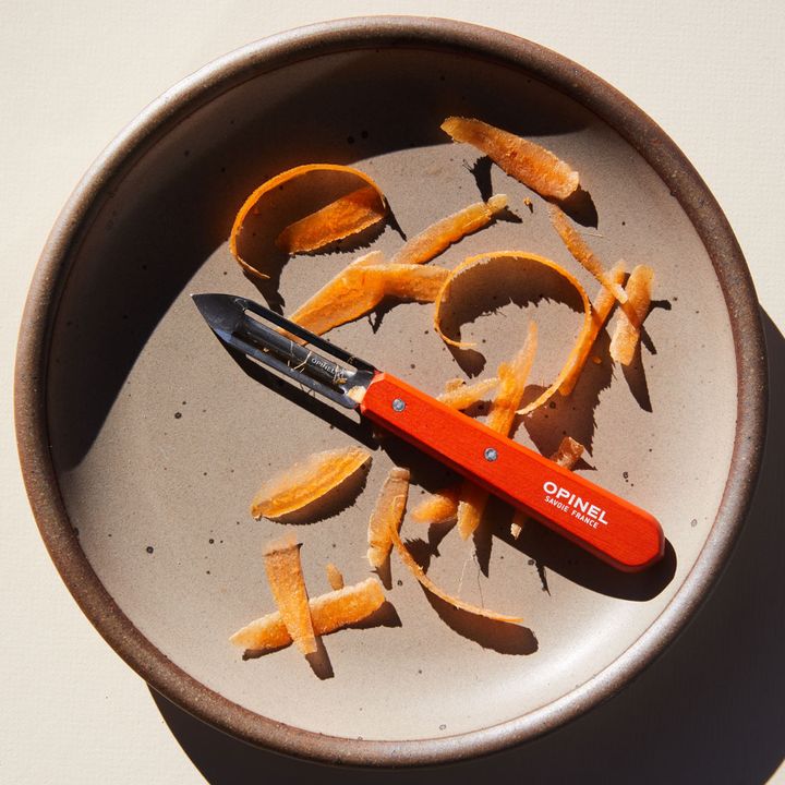 East Fork pottery dinner plate in Morel with stainless steel vegetable peeler with orange handle on top, surrounded by carrot peels.