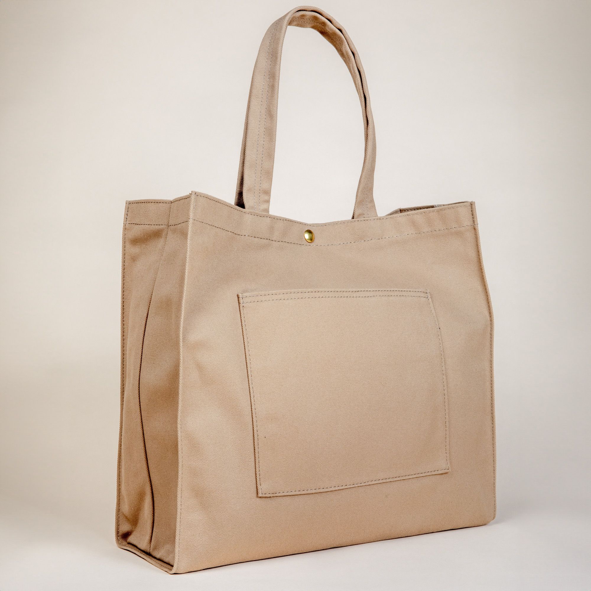 The back of a sturdy canvas tan tote bag with handles, flat pocket and a metal closure button at the top.