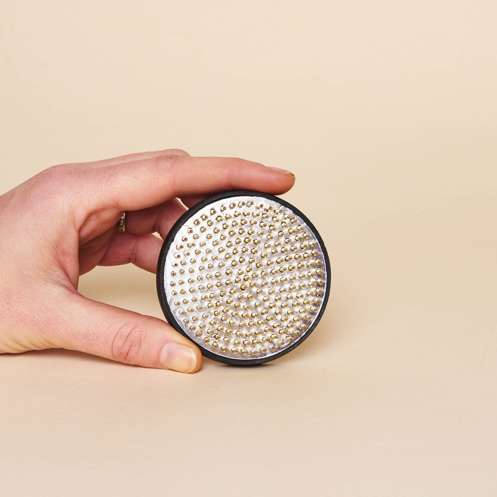 A hand holding a medium "kenzan" – a pin frog made of brass spikes on a flat circular base to assist in flower arrangements.