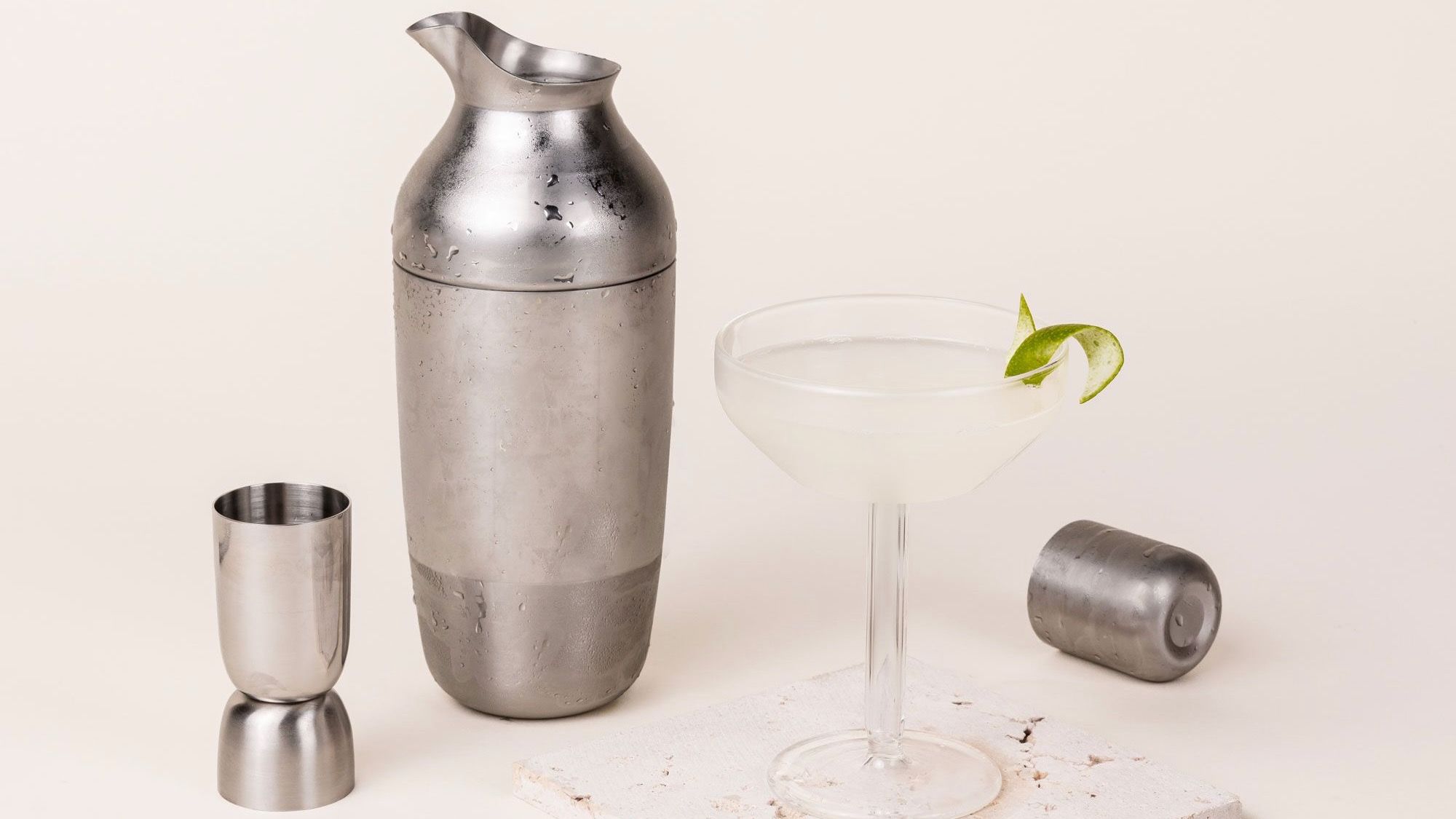 The Mescola Cocktail Set (including a stainless steel shaker, jigger, and cocktail spoon) with a fresh martini in a coupe glass
