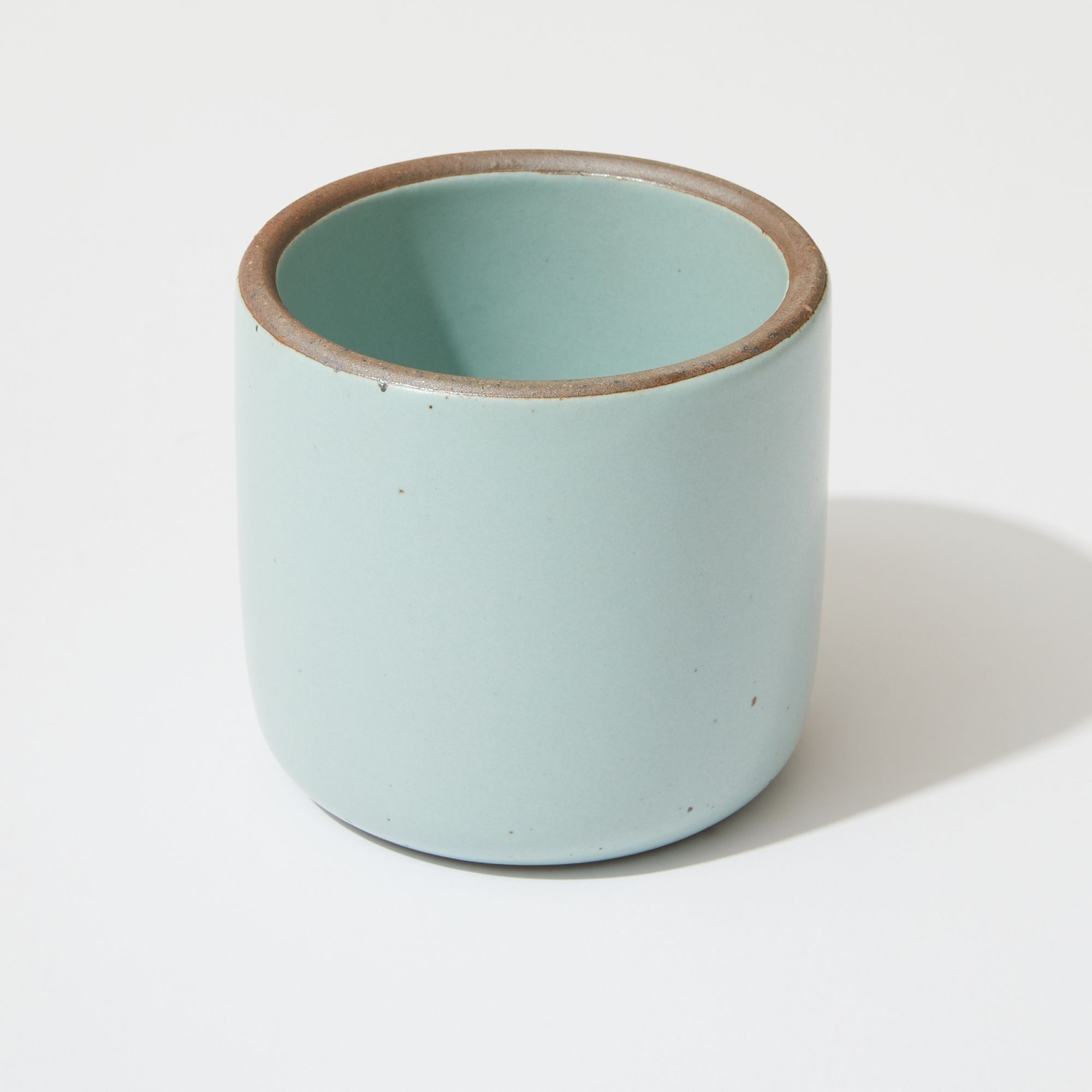 A ceramic cup in a pale turquoise color with a raw unglazed rim