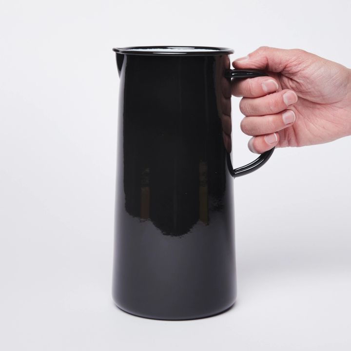 Hand holding the handle on the right side of a shiny black cylindrical jug with a spout on the left