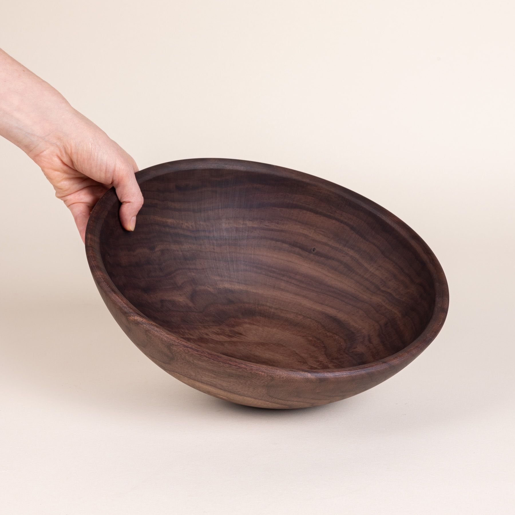 A hand holds out a large walnut wood bowl