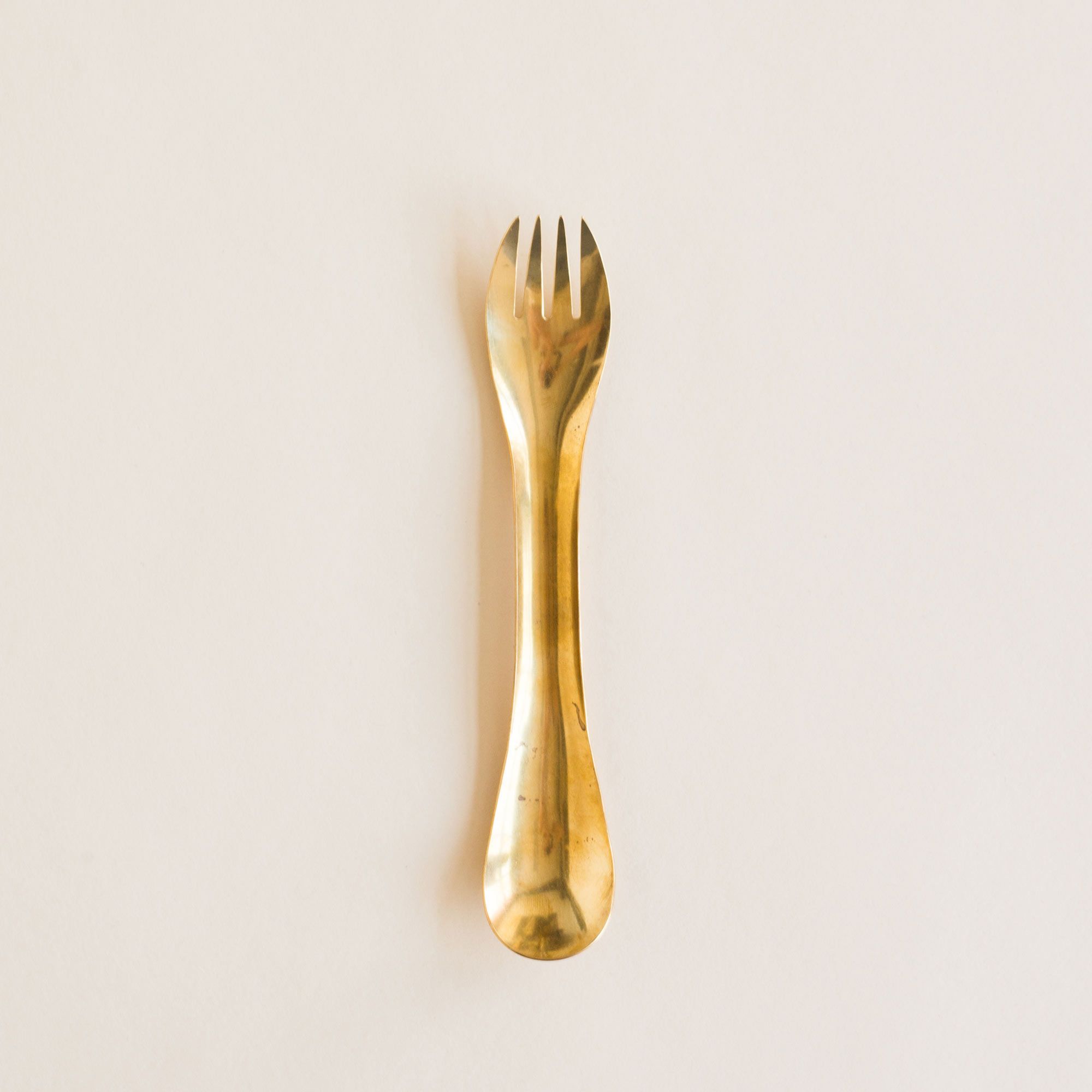 A spork, or eating utensil with spoon at one end and fork at the other, and made of brass