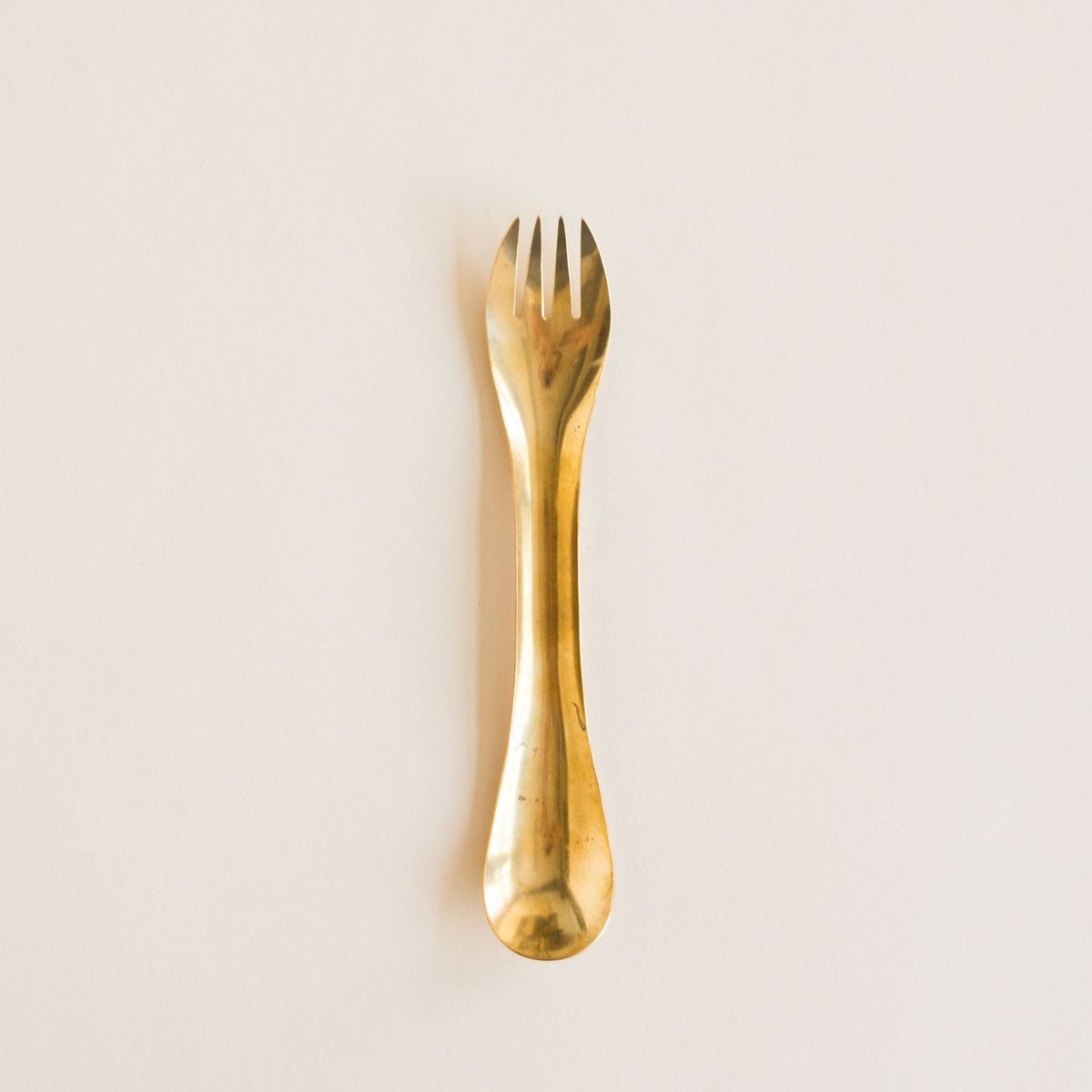 A brass spork: an eating utensil with spoon at one end and fork at the other