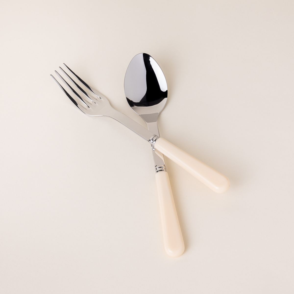 A serving size spoon and fork in a shiny steel with a matte cream handle