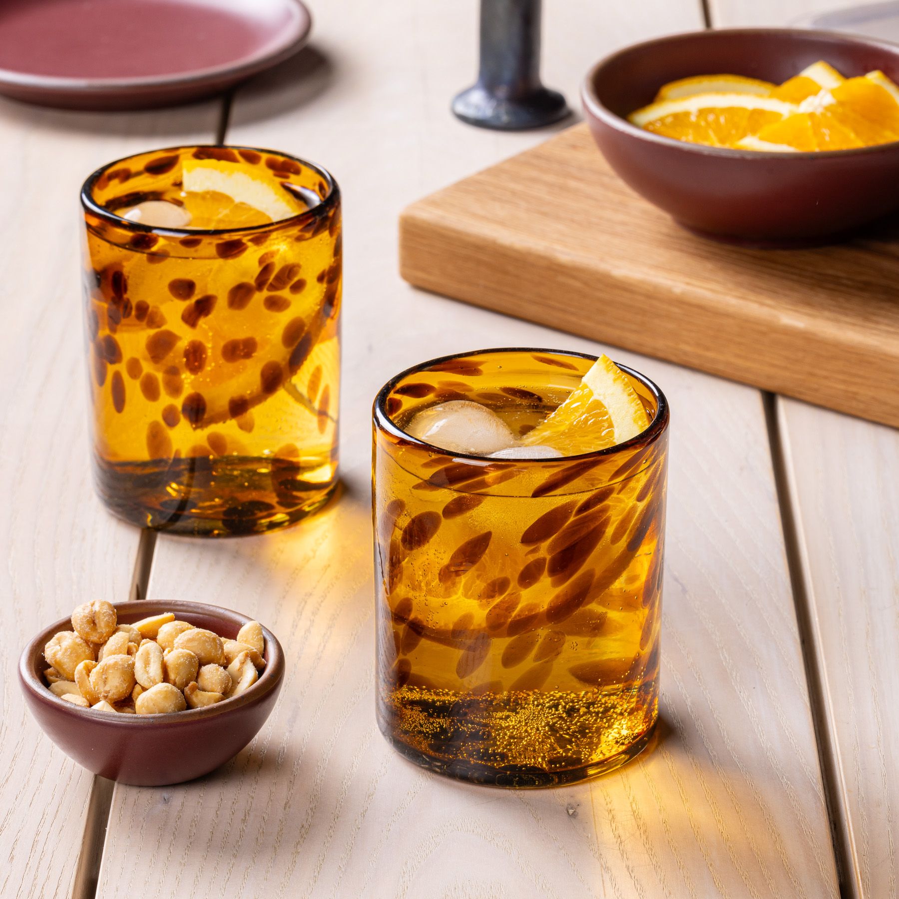 2 tortoiseshell drinking glasses filled with a drink and sitting on a table with a tiny bowl of nuts