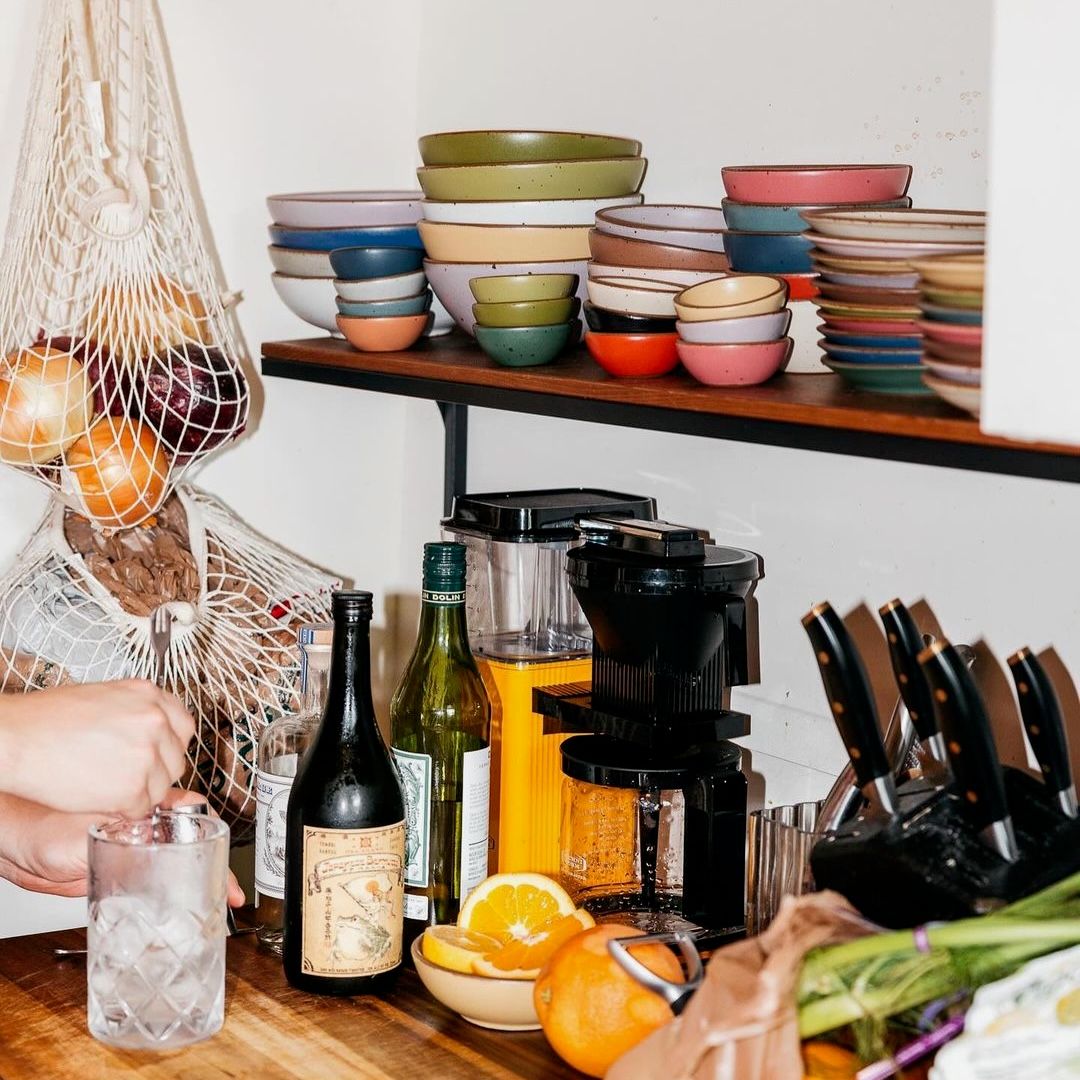 In a kitchen corner is a shelf of colorful ceramic bowls and plates, and cooking utensils and tools.