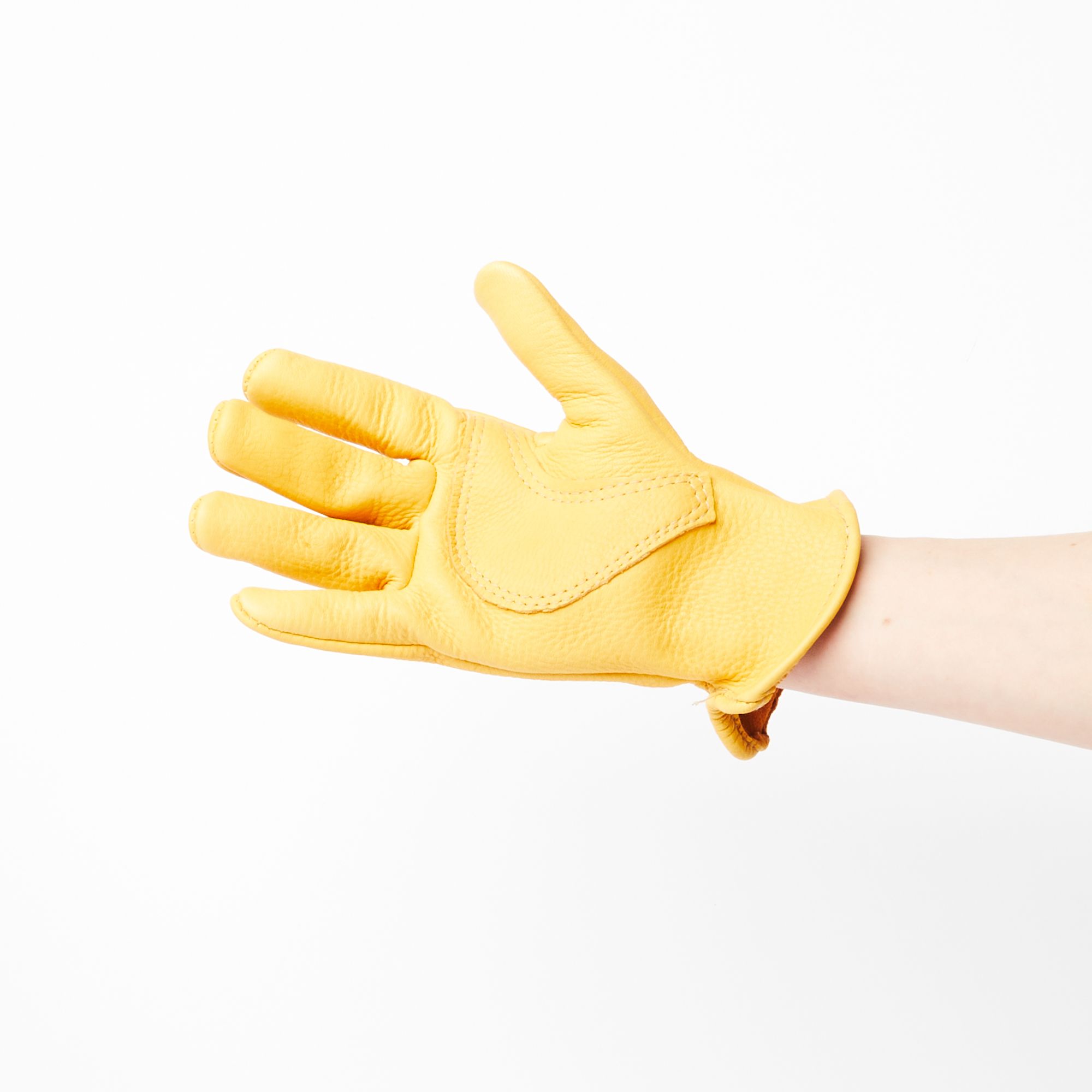 A hand wearing one buttery yellow deerskin garden glove