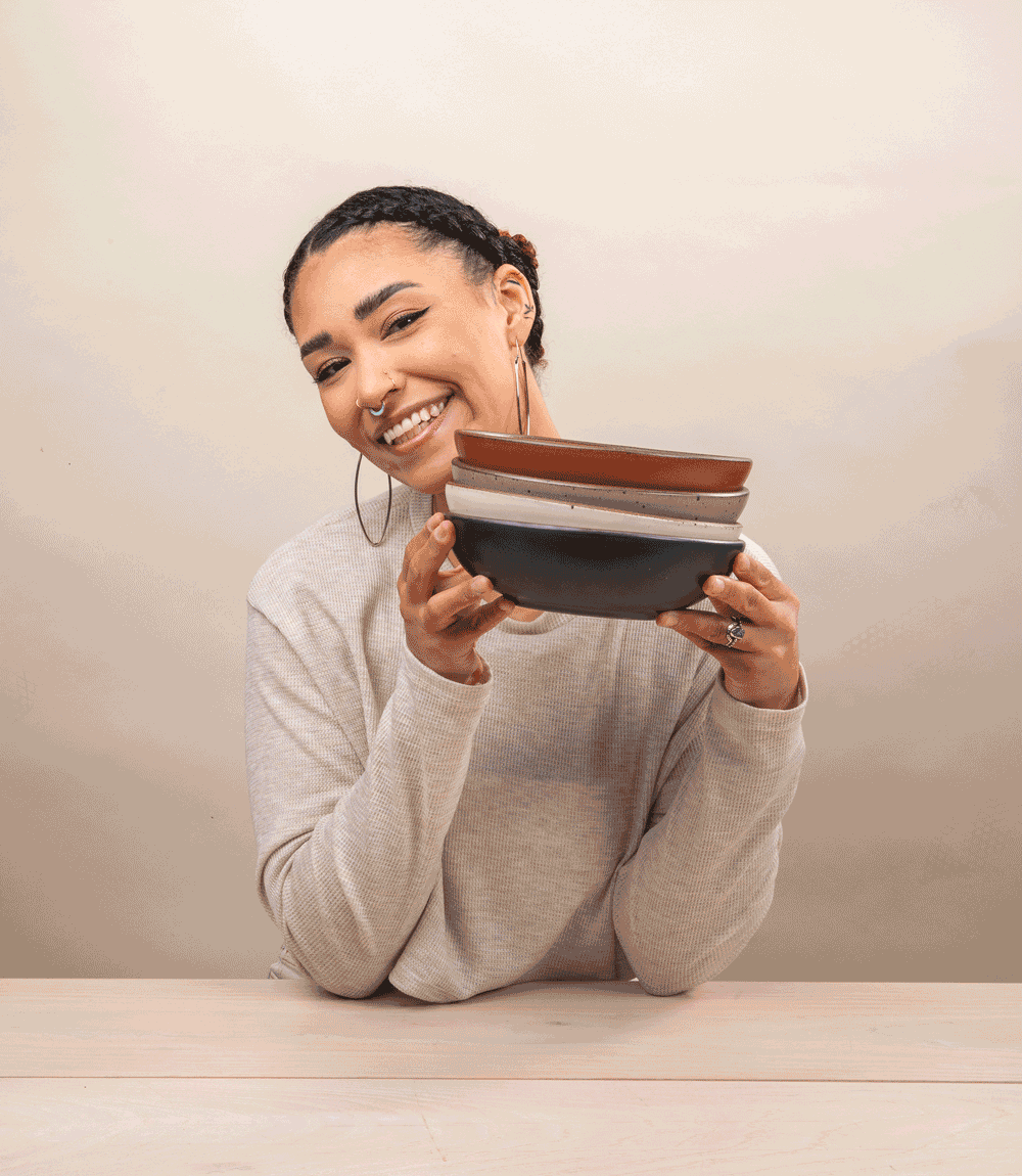 A gif of a woman holding a stack of ceramic shallow bowls and smiling