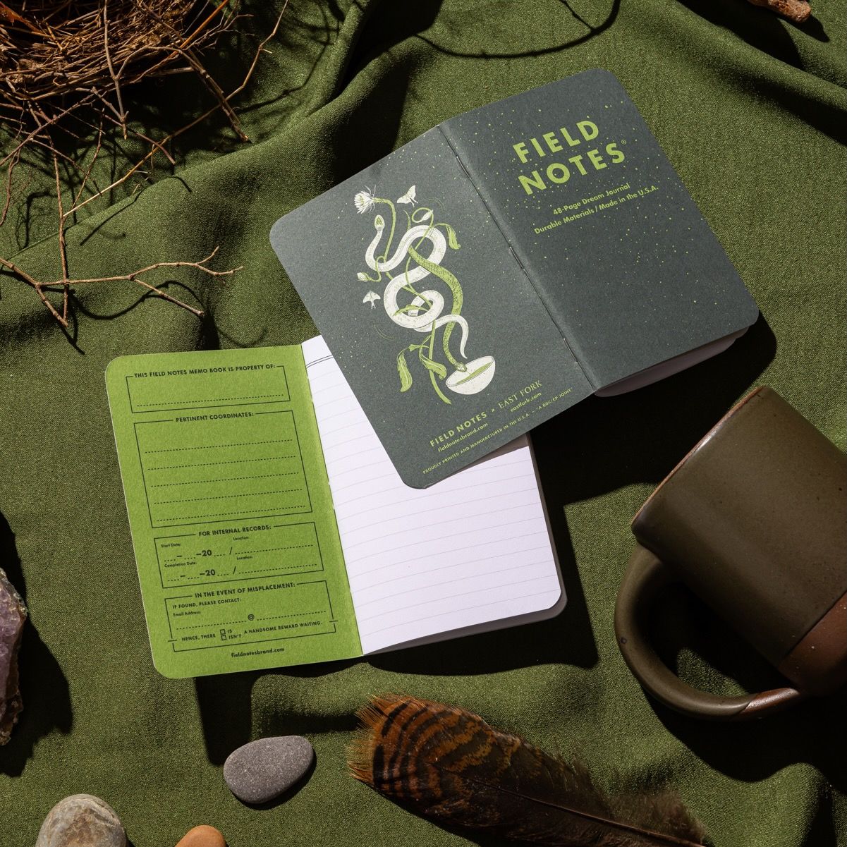 An artful layout of 2 journals both open, one right side up, one laying flat closed. Both in a forest green color against a green background next to a forest green mug.