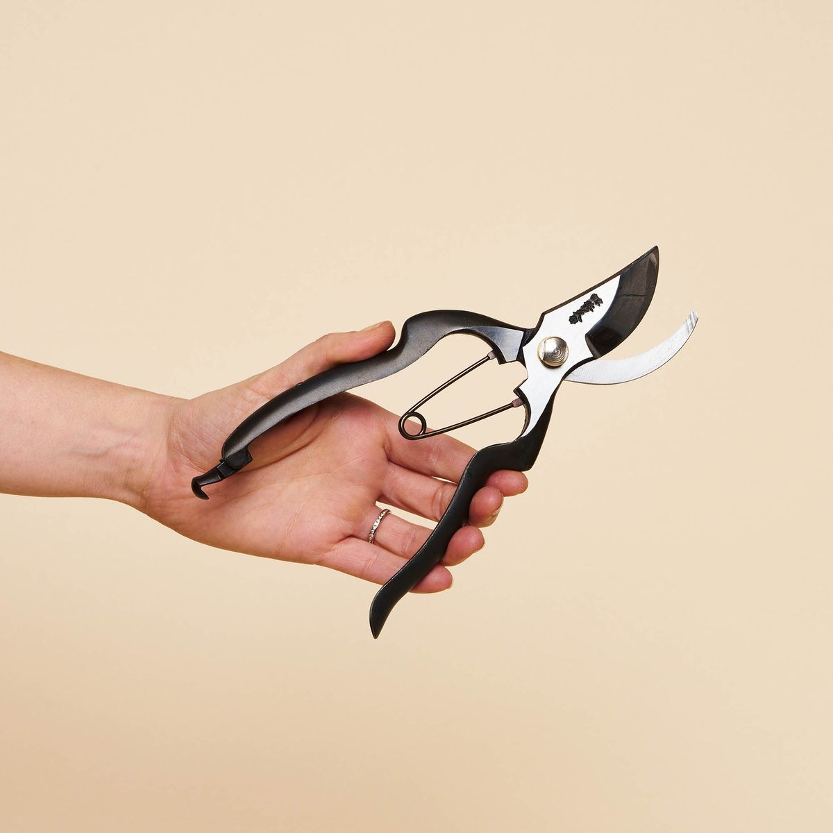 A hand holding sharp gardening pruning shears with a black handle