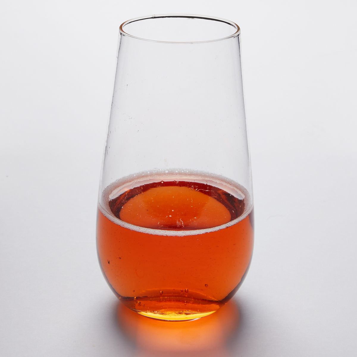 One clear stemless champagne glasses that taper slightly toward the rim, filled halfway with a bubbly amber drink