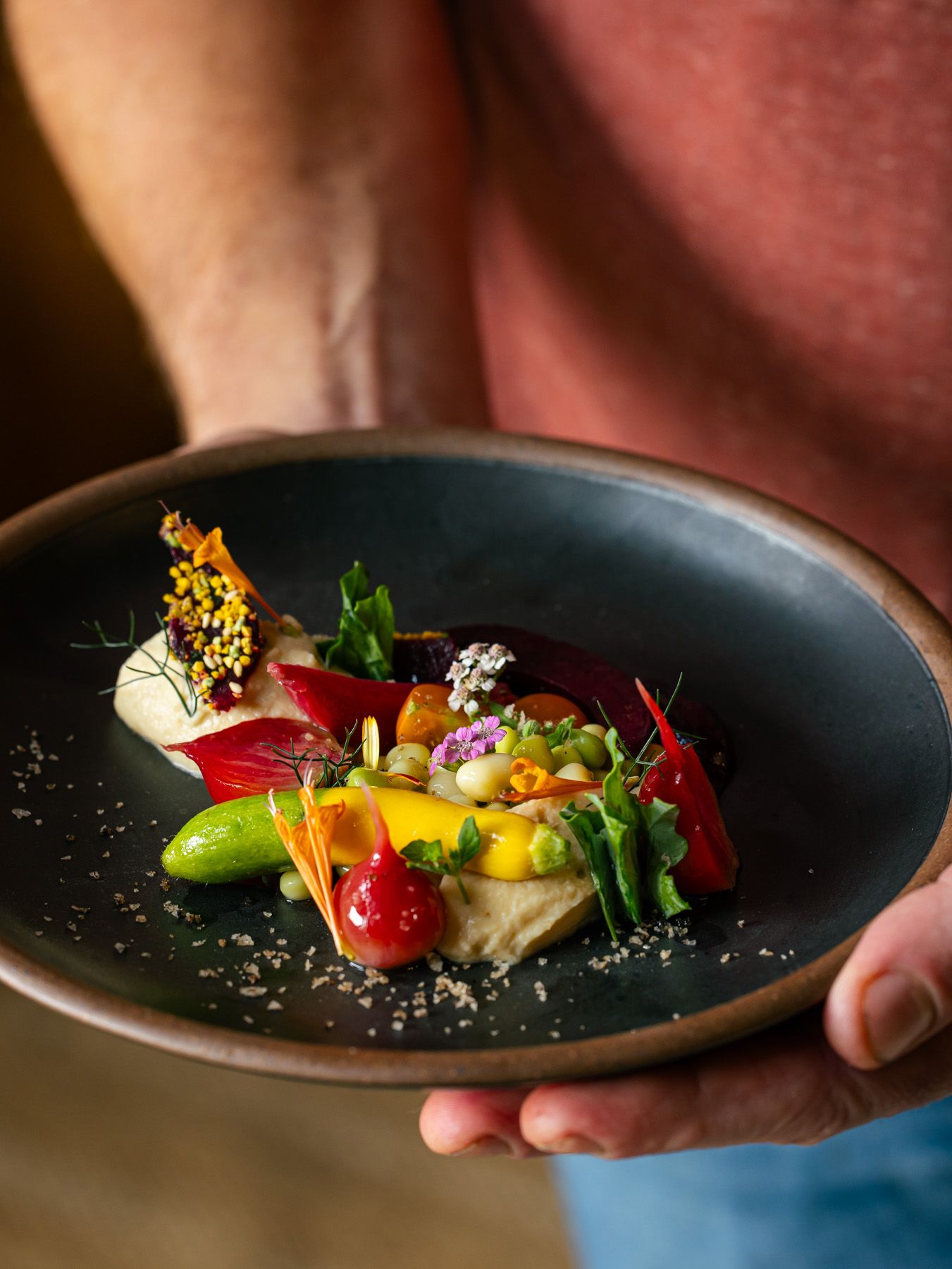 A black ceramic plate has a beautiful colorful dish on top with fresh vegetables