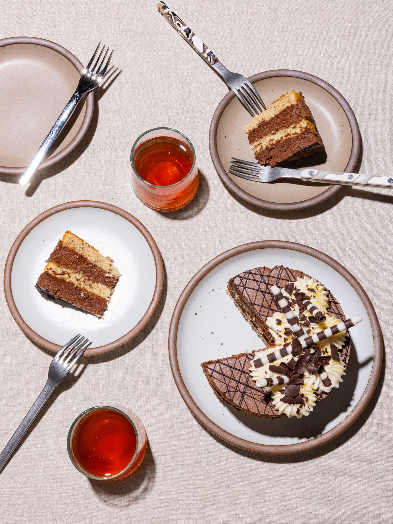 Various ceramic plates in neutral colors with dessert on top with glasses of red punch and silverware.