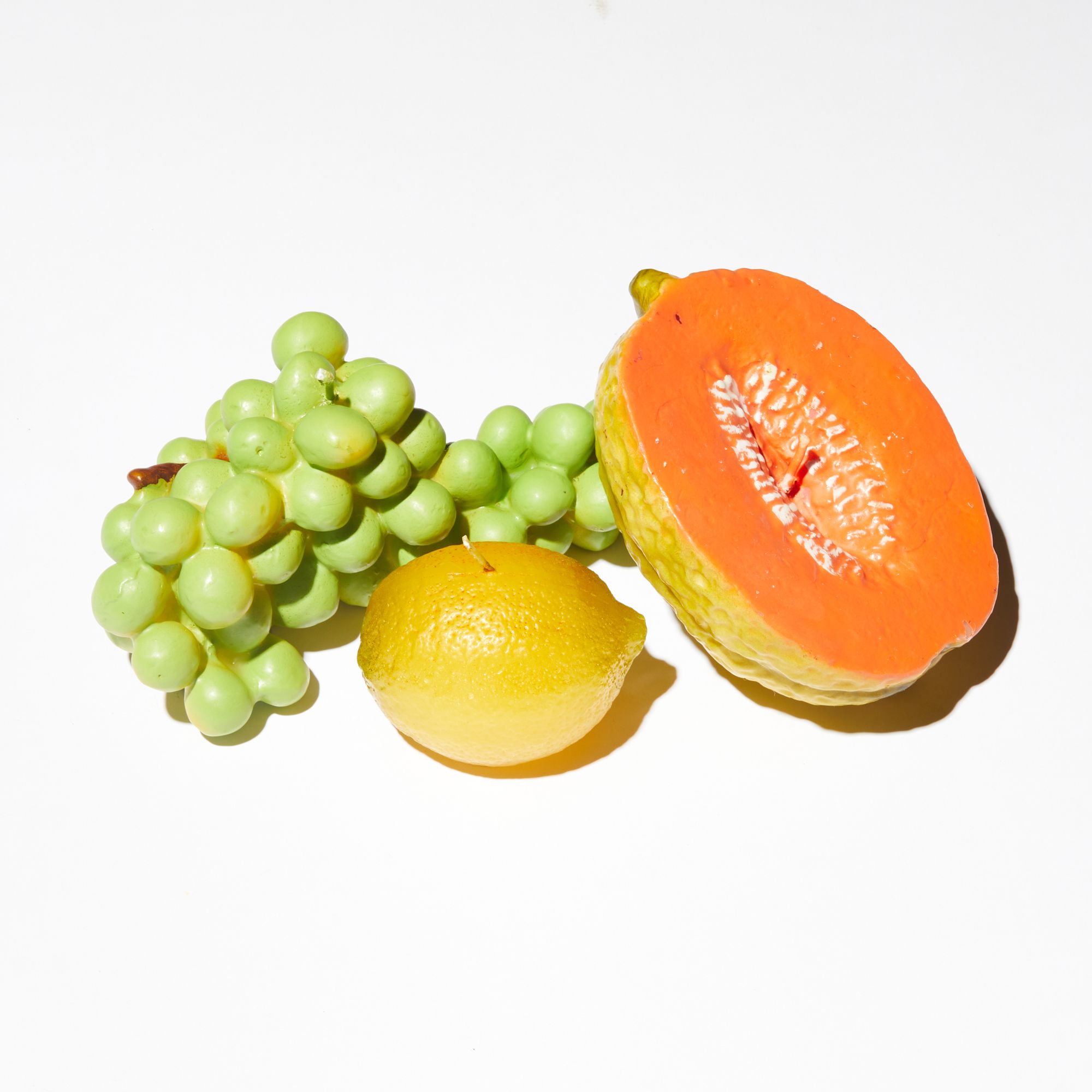 Three candles made in the likeness of a halved cantaloupe, a lemon and a bunch of green grapes 