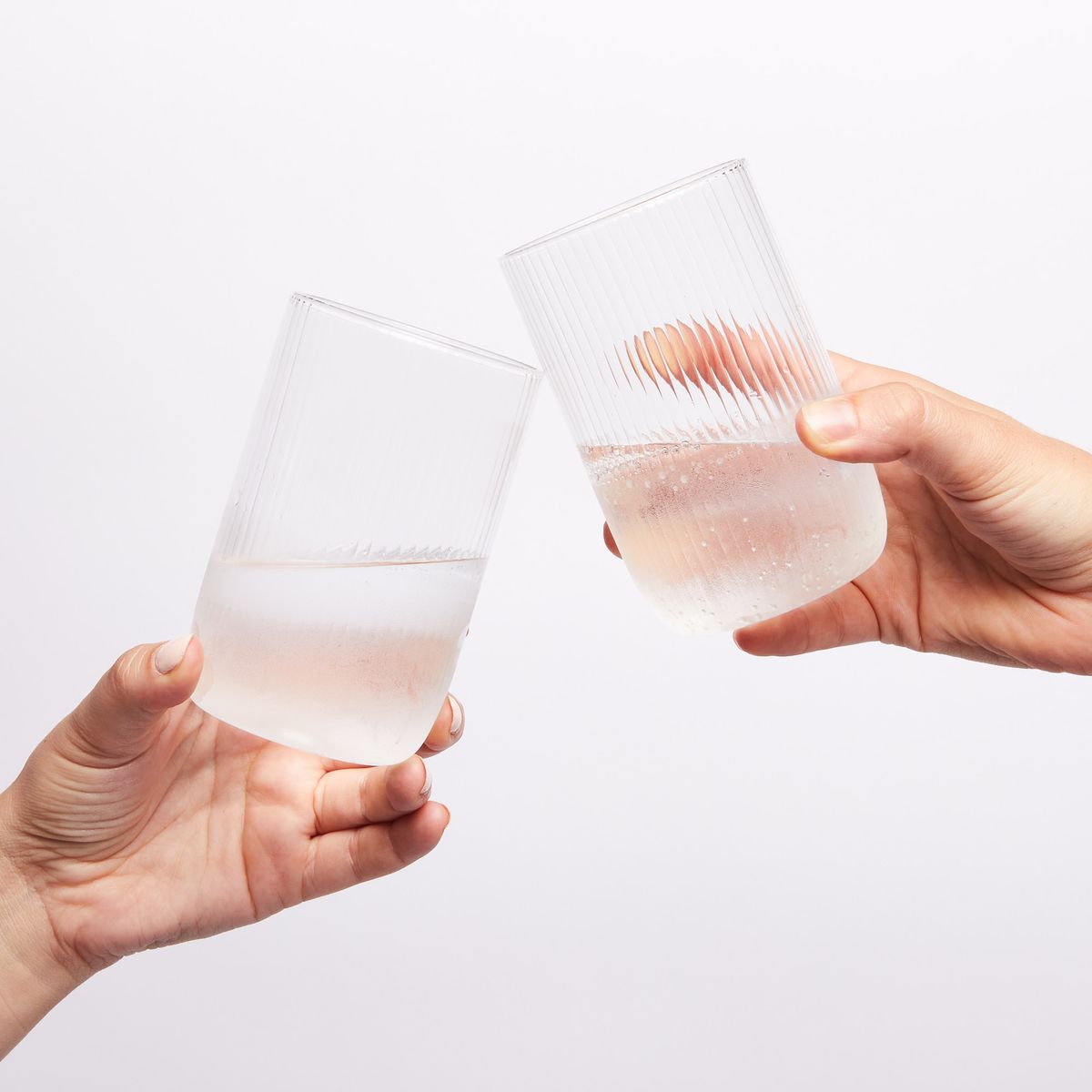 two hands holding two glasses half full of water towards each other