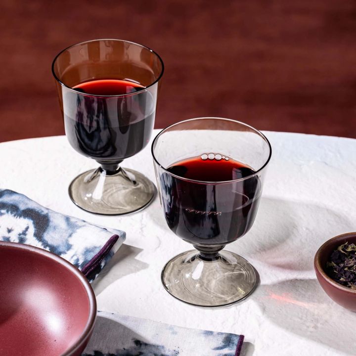 2 short wine glasses with an angular cup and grey color filled with red wine on a table