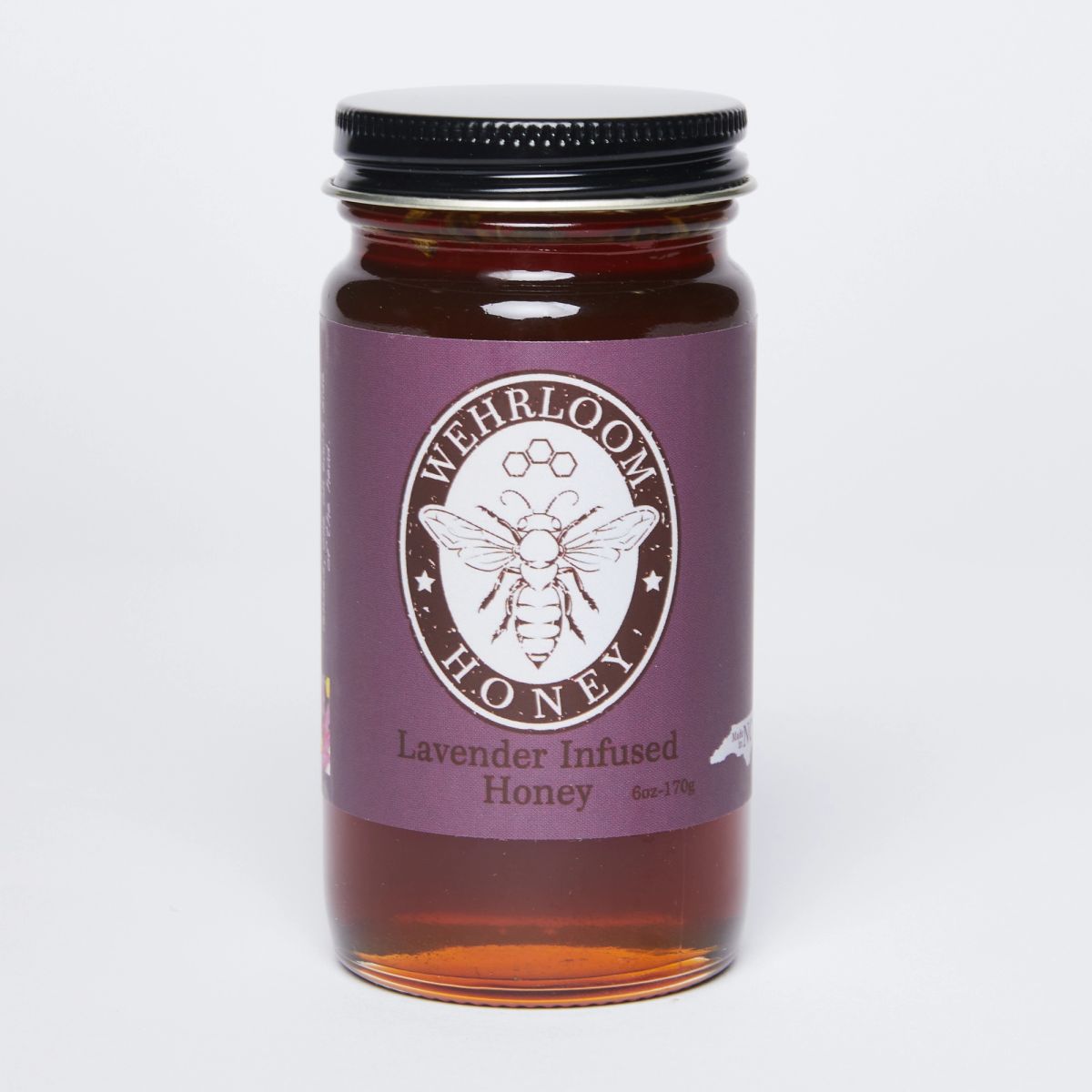 Glass jar filled with golden honey with a black lid and purple label that reads 'Lavender infused honey''.