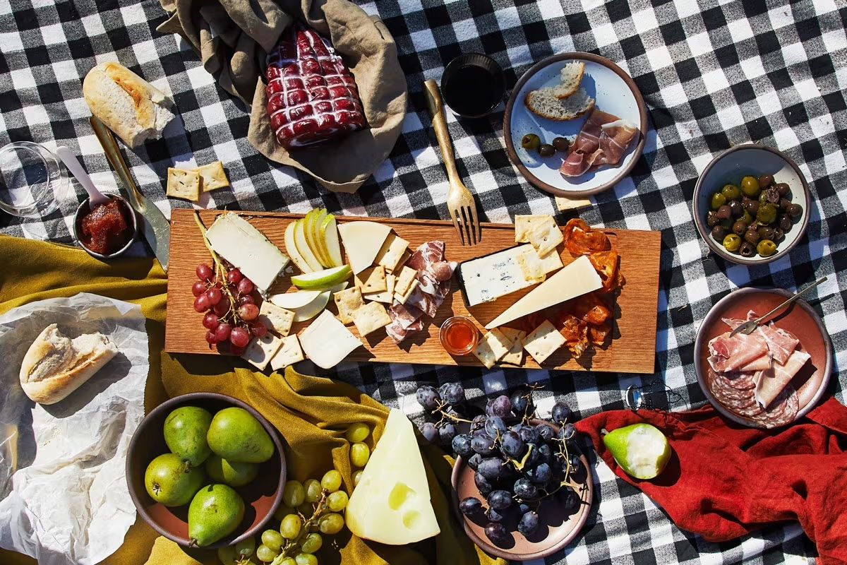 A wood charcuterie board filled with cheeses, fruits, and more, with bowls and plates surrounding